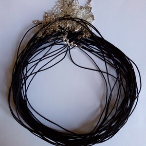May include: A pile of black cord necklaces with silver clasps. The cords are bundled together and the clasps are visible at the top of the pile.
