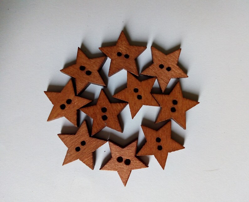May include: Ten wooden star-shaped buttons in a warm brown hue. Each button features two small black holes for sewing. The buttons are arranged in a circular pattern against a white backdrop, ideal for craft projects.