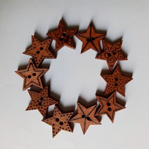 May include: A circular arrangement of wooden star-shaped buttons. Each button is a warm brown colour with a star shape and two holes for sewing. Some stars have decorative etched patterns.