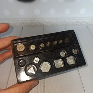 Puede incluir: Una bandeja de pl&aacute;stico negro con un juego de pesas de plata para una balanza. Las pesas son de varios tama&ntilde;os y formas, algunas marcadas con n&uacute;meros como "500" y "900".