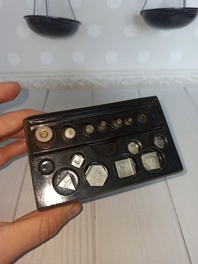 Puede incluir: Una bandeja de pl&aacute;stico negro con un juego de pesas de plata para una balanza. Las pesas son de varios tama&ntilde;os y formas, algunas marcadas con n&uacute;meros como "500" y "900".