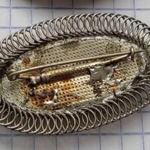May include: A silver oval brooch with a decorative wire design and a silver pin on the back.