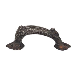 Könnte beinhalten: Ein gebogener Schubladengriff im Vintage-Stil mit einem verzierten Design. Der Metallgriff hat eine dunkle, antike Bronzefarbe und weist dekorative Schnörkel und eine strukturierte Oberfläche auf. Die Enden haben eine klauenartige Form.