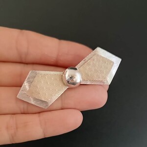 May include: A silver brooch with a geometric design and a round ball in the center.