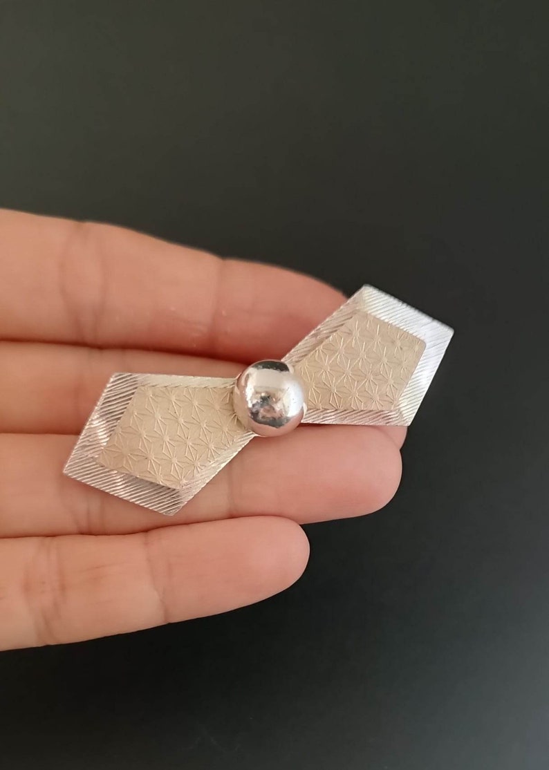 May include: A silver brooch with a geometric design and a round ball in the center.