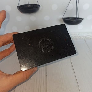 Puede incluir: Caja rectangular negra con un logotipo circular rojo que dice "Precision Ground" y "Made in England".