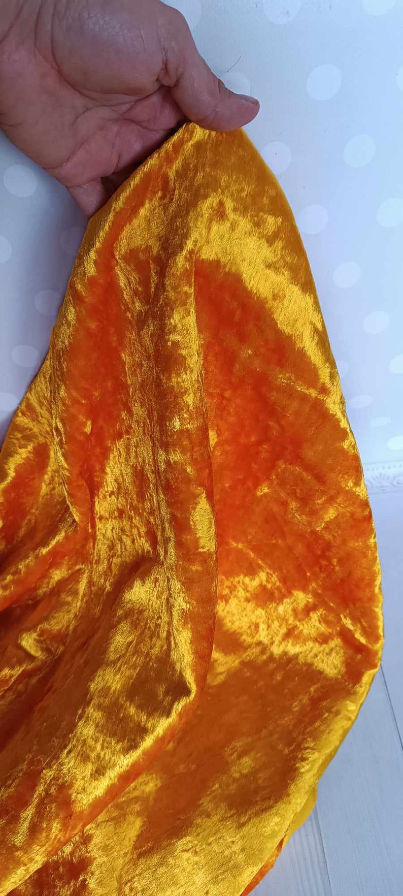 May include: A bright orange velvet fabric with a soft, plush texture. The fabric is folded and draped over a hand.