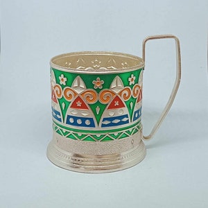 May include: Silver-plated cup holder with a green, orange, red, blue, and white geometric design. The cup holder has a handle and a textured base.