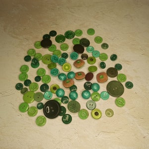 May include: A collection of various green buttons in different shades and sizes. The buttons include round, square, and textured designs, with some featuring two or four holes. The color palette ranges from light lime to deep forest green.