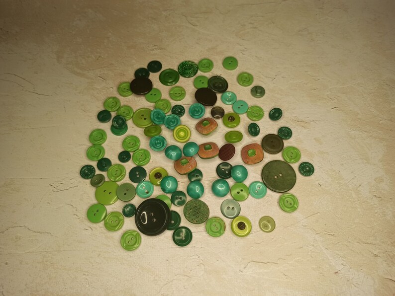 May include: A collection of various green buttons in different shades and sizes. The buttons include round, square, and textured designs, with some featuring two or four holes. The color palette ranges from light lime to deep forest green.