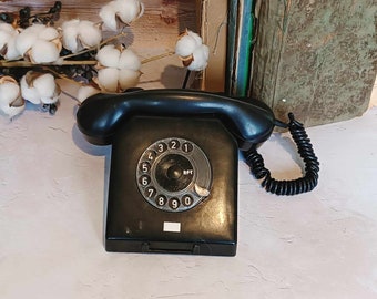 May include: A black rotary dial phone with a white dial face and black cord. The phone has a black receiver and a black base.