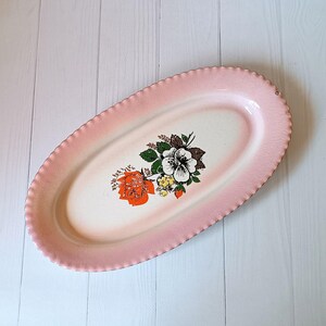 Puede incluir: Un plato ovalado de servir rosa con un diseño floral blanco. Las flores son de color naranja, blanco y verde.