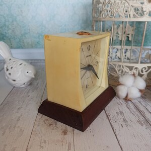May include: A vintage cream-colored alarm clock with a brown base. The clock face has black hands and black numbers. The clock says "Sevan" on the face.
