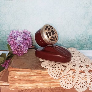 May include: A vintage microphone with a brown base and a silver grill. The microphone is sitting on a stack of old books with a crocheted doily.