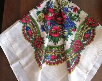 Pode incluir: Um lenço quadrado de algodão branco com um padrão floral colorido. O padrão apresenta flores vermelhas, cor-de-rosa, amarelas, verdes e azuis com uma borda verde, amarela e vermelha.