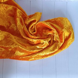 May include: A bright yellow velvet fabric draped on a white wooden surface. The fabric is soft and luxurious, with a subtle sheen.