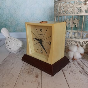 May include: A vintage cream-colored alarm clock with a black face and black hands. The clock has a brown wooden base and says "Seiko" on the face.