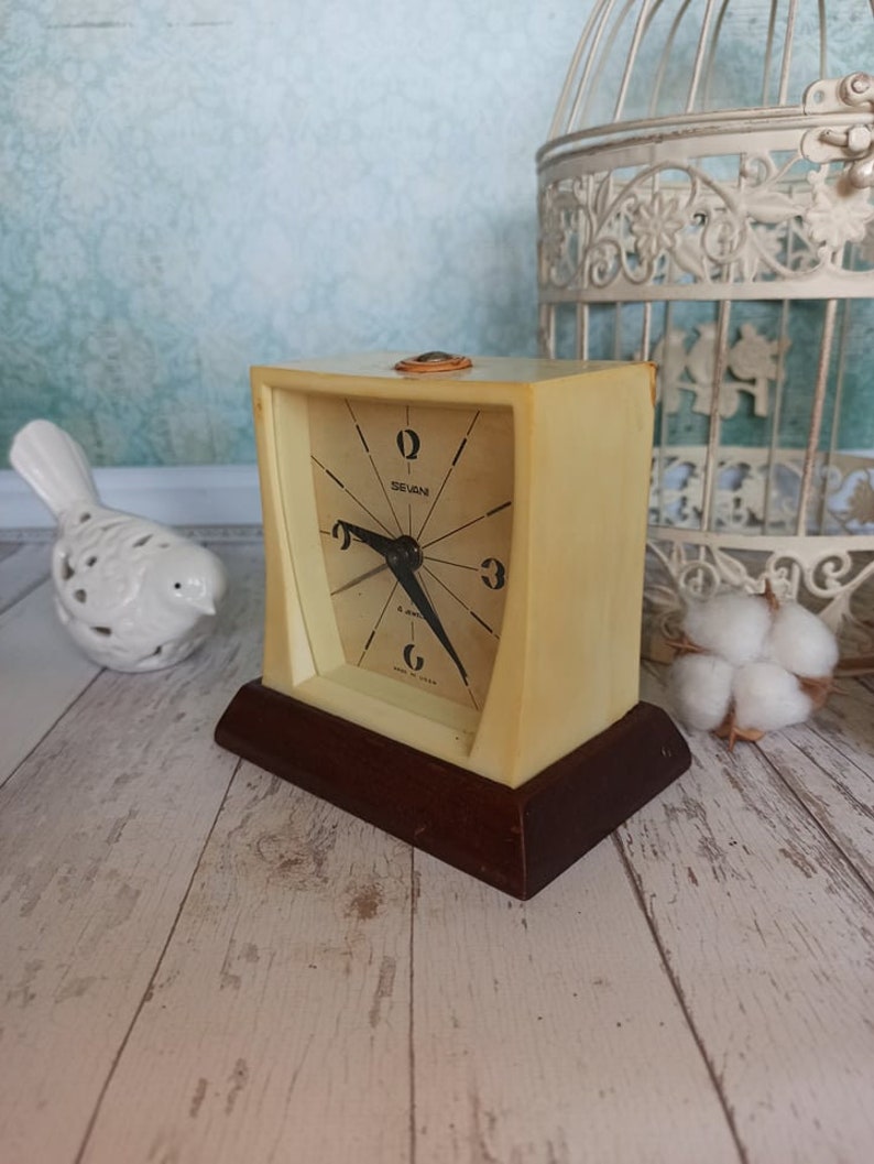 May include: A vintage cream-colored alarm clock with a black face and black hands. The clock has a brown wooden base and says "Seiko" on the face.