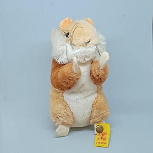May include: A brown and white plush hamster toy sitting up with its paws raised. The toy has a small yellow tag attached to its foot with the text "Steiff" and "2150/12" on it.