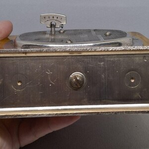 May include: A vintage silver-toned music box with a turntable design. The box has a rectangular base with a silver frame and a wooden top. The turntable has a silver arm and a small handle. The word "TORVC" is visible on the handle.