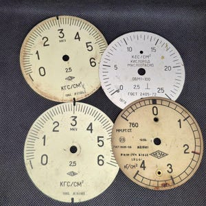 Pode incluir: Quatro mostradores de calibre vintage com algarismos e marcações pretas sobre um fundo creme. Cada mostrador circular tem um orifício central e vários textos, incluindo "KГC/CM²" e números.