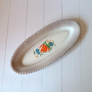 Peut inclure: Un plat de service ovale blanc avec un bord festonné et un motif floral avec des fleurs orange, bleues et vertes.