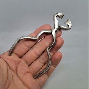 Peut inclure: Un casse-noix argenté au design unique. Le casse-noix présente un corps incurvé et deux têtes décoratives en haut. Les poignées sont incurvées et ergonomiques, et le design général est vintage.