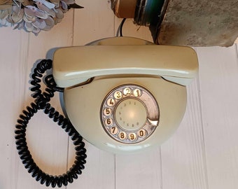 May include: A vintage rotary dial phone with a cream-colored body and a black coiled cord. The phone has a circular dial with black numbers and a white center.