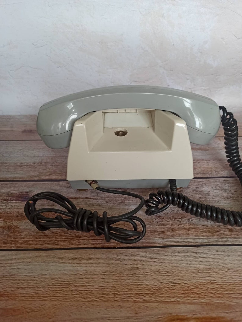 May include: A vintage rotary dial phone with a gray handset and a white base. The phone has a coiled cord and a separate black cord.