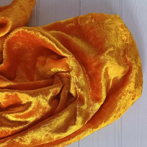 May include: A bright yellow velvet fabric draped over a white wooden surface. The fabric is soft and plush, with a subtle sheen.