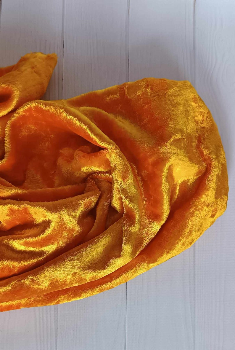 May include: A bright yellow velvet fabric draped over a white wooden surface. The fabric is soft and plush, with a subtle sheen.
