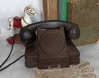 May include: A vintage brown rotary dial phone with a black receiver and a white crocheted doily underneath. The phone is sitting on a white wooden surface with a rocking horse toy in the background.