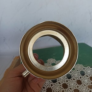 May include: The bottom of a silver metal cup with a round opening. The cup has a handle on the side.