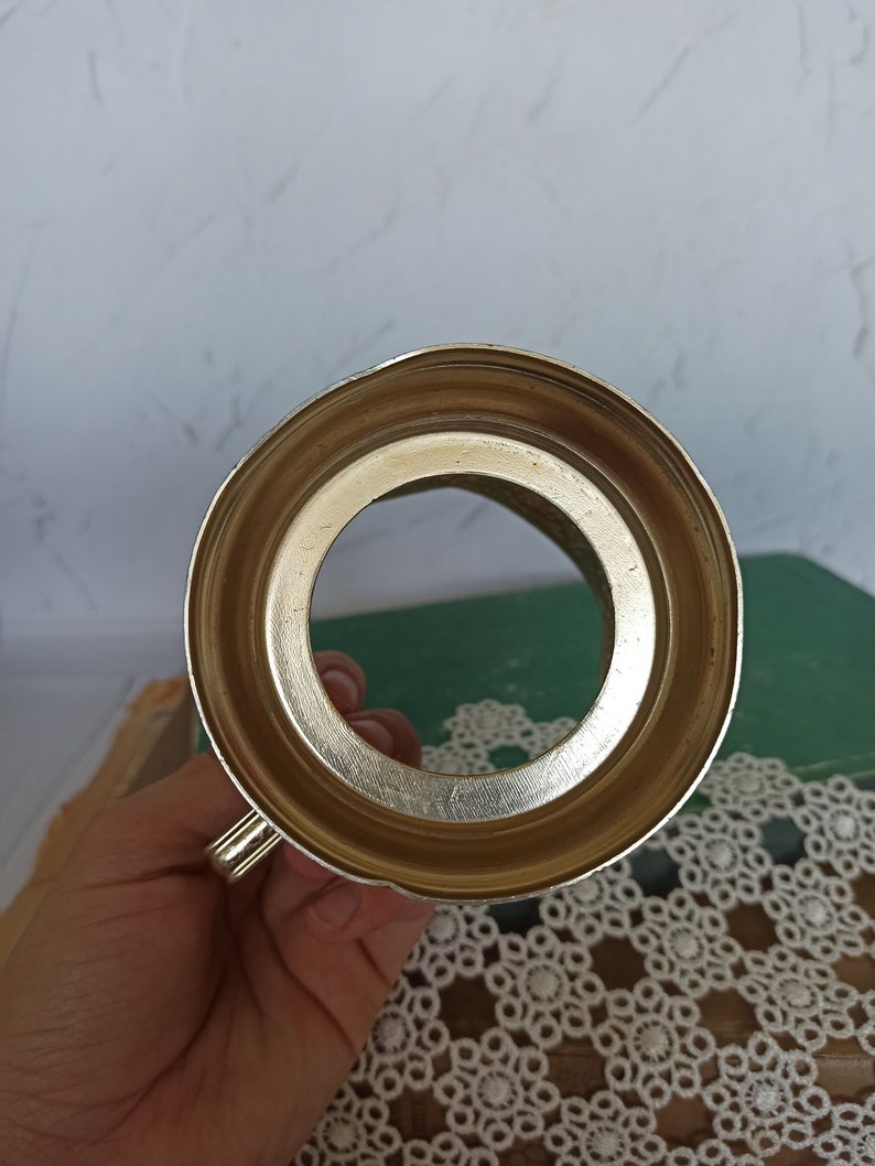 May include: The bottom of a silver metal cup with a round opening. The cup has a handle on the side.