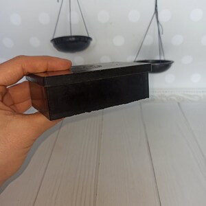 Puede incluir: Una caja rectangular negra con una tapa ligeramente elevada. La caja est&aacute; hecha de un material liso y duro y tiene un brillo sutil. La caja est&aacute; siendo sostenida en una mano, pero la mano no es visible en la imagen.