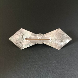 May include: Silver bow brooch with a textured design and a pin on the back.