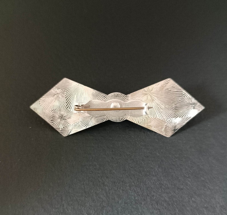 May include: Silver bow brooch with a textured design and a pin on the back.