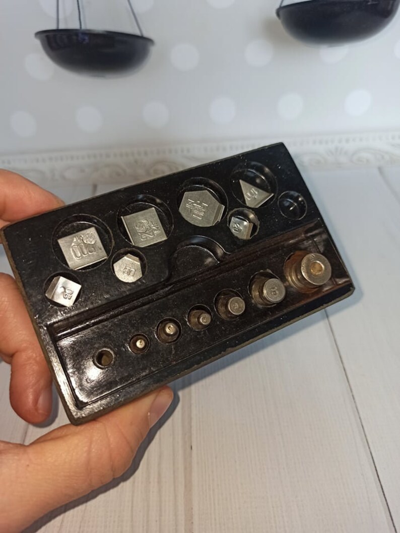 Puede incluir: Una caja de pl&aacute;stico negro con un juego de pesas de plata para una balanza. Las pesas son de diferentes formas y tama&ntilde;os, y est&aacute;n etiquetadas con su peso en gramos.