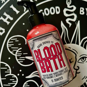 May include: A red bottle of "Blood Bath" scented body wash and bubble bath by Sugar Shower Co. The bottle is labeled with a black and white design and the text "Scented Body Wash/Bubble Bath Red Currant | Berries | Roses 6 Ounces".