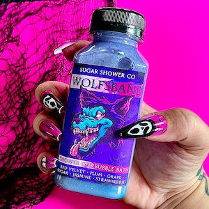 Puede incluir: Una botella azul de gel de ducha con un gráfico de cabeza de lobo y el texto "SUGAR SHOWER CO WOLFSBANE SHOWER GEL BUBBLE BATH RED VELVET PLUM GRAPE SUGAR JASMINE STRAWBERRIES".