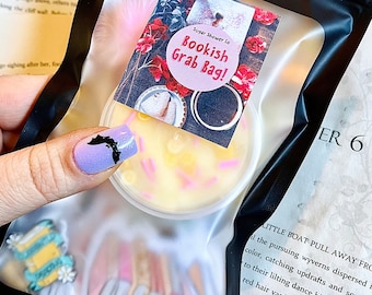 May include: A clear plastic bag containing a round container with yellow wax and pink sprinkles, labeled "Bookish Grab Bag!" The bag also contains book-themed embellishments. The background includes text from a book.