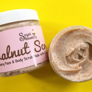 Puede incluir: Dos frascos de plástico transparente de "Walnut Scrub" sobre un fondo amarillo. Los frascos tienen tapas blancas y etiquetas rosas con el texto "Sugar Shower Co." y "Creamy Face & Body Scrub Made With Cream". Un frasco está abierto, revelando el aspecto texturizado y marrón claro del exfoliante.