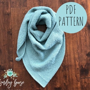 May include: A teal blue crocheted scarf with a textured stitch pattern. The scarf is folded and displayed on a wooden surface. The text "PDF PATTERN" is written in white on a light blue circle.