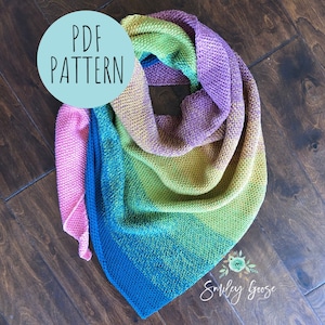 Könnte beinhalten: Ein farbenfroher Häkel-Schal mit einem Farbverlauf von Rosa, Blau, Grün und Lila. Der Schal ist gefaltet und auf einer Holzoberfläche abgelegt. Ein Kreis mit dem Text "PDF PATTERN" befindet sich in der oberen linken Ecke des Bildes. Der Text "Smiley Goose" befindet sich in der unteren rechten Ecke des Bildes.