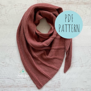 May include: A dusty rose-colored knitted shawl with a triangular shape. The shawl has a ribbed texture and is draped on a light wood-grain surface. A light blue circle with the text "PDF PATTERN" is in the image.