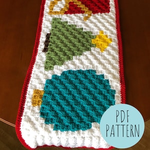 Op de afbeelding: Haakpatroon voor een kersttafelkleed met een witte achtergrond en rode, groene, gele en blauwe ornamenten en bomen. De tekst "PDF PATTERN" staat in een cirkel in de rechterbenedenhoek van de afbeelding.