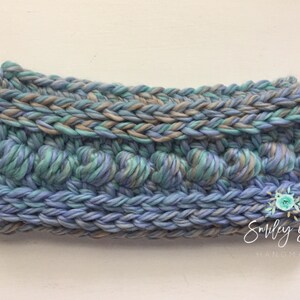 Puede incluir: Una diadema de crochet azul, verde y marr&oacute;n con un dise&ntilde;o texturizado. La diadema est&aacute; hecha por Smiley Goose Handmade.