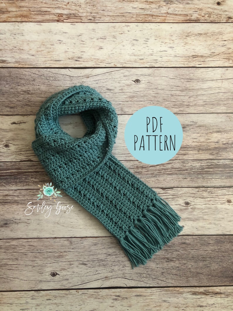 May include: A teal crochet scarf with fringe on the ends. The scarf is laid out on a wooden surface. A circle with the text "PDF PATTERN" is in the background.