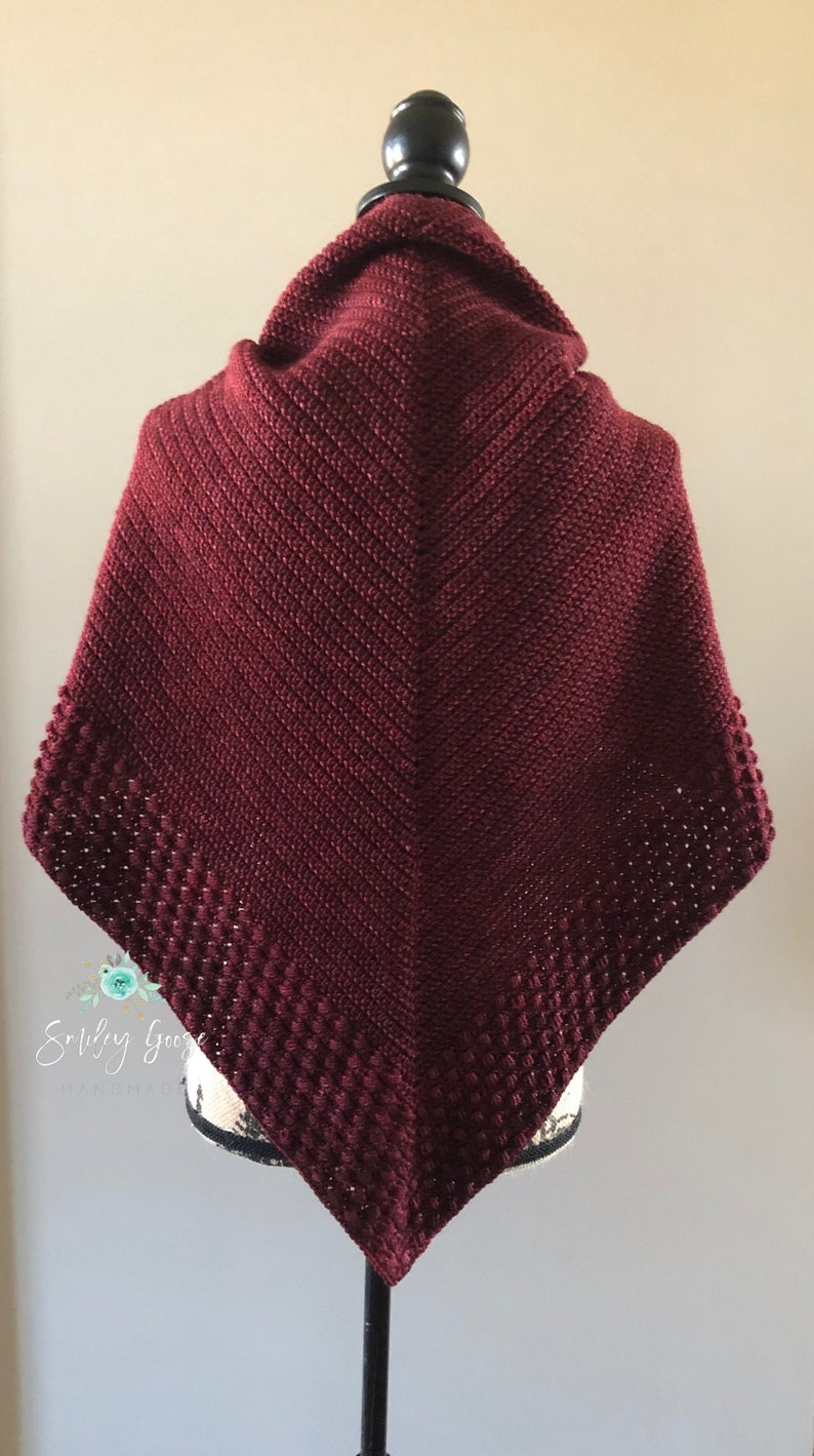 May include: A burgundy crocheted shawl with a textured border. The shawl is draped over a black mannequin.