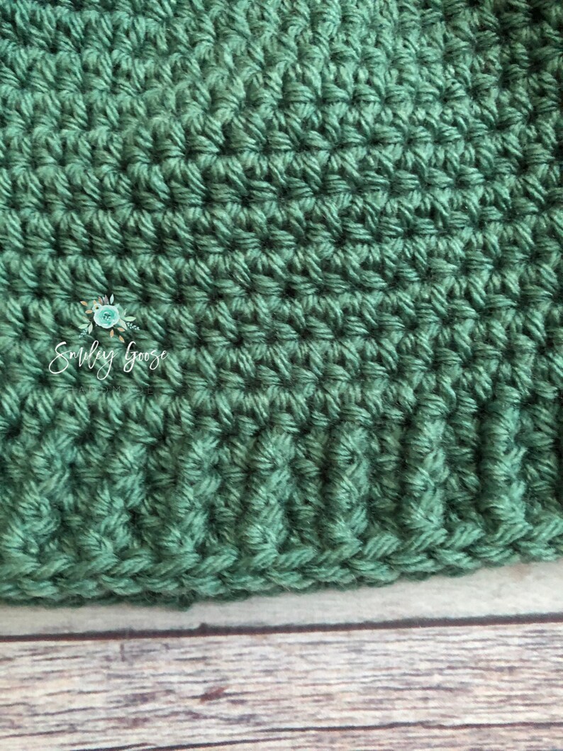 May include: Close-up of a green crocheted fabric with a textured pattern. The fabric is made with a single crochet stitch and has a smooth, even texture.